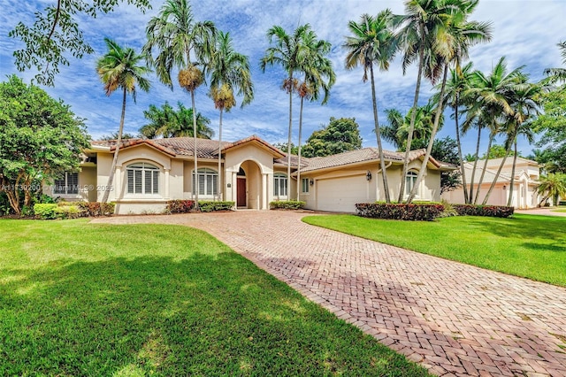 mediterranean / spanish house featuring a garage, a tile roof, a front lawn, and stucco siding