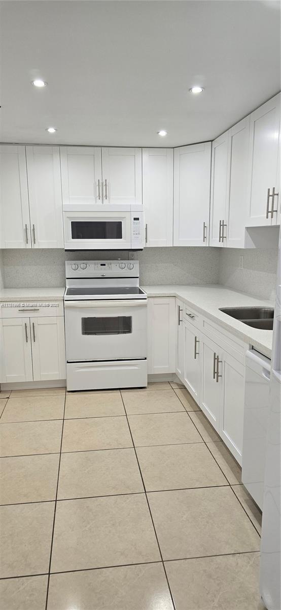 kitchen featuring white appliances, light tile patterned floors, white cabinets, and a sink