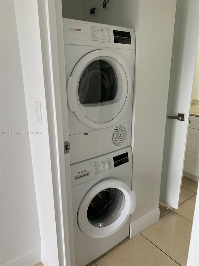 clothes washing area featuring stacked washing maching and dryer, baseboards, light tile patterned floors, and laundry area