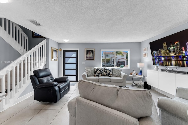 living room featuring stairs, light tile patterned floors, a textured ceiling, and visible vents