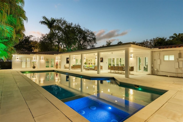 6784 SW 97th St, Pinecrest, FL 33156 - pool at dusk featuring french doors, a patio area, outdoor lounge area, and a pool with connected hot tub