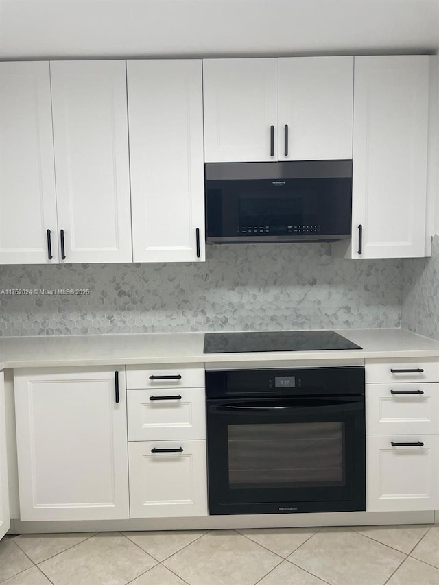 kitchen featuring light tile patterned floors, tasteful backsplash, light countertops, white cabinetry, and black appliances