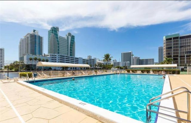 pool with a patio area, a city view, and fence