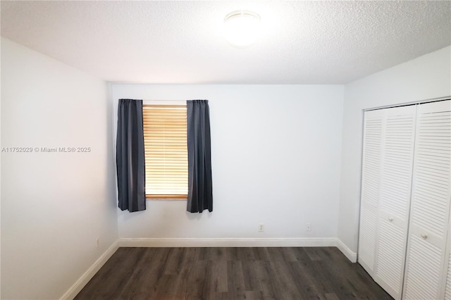 unfurnished bedroom featuring a closet, dark wood finished floors, a textured ceiling, and baseboards