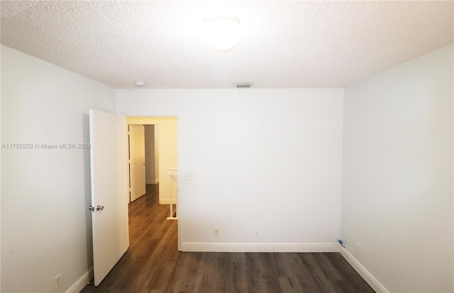 empty room featuring dark wood-type flooring, visible vents, a textured ceiling, and baseboards