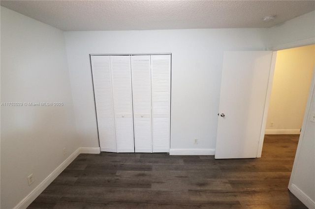 unfurnished bedroom with a textured ceiling, a closet, wood finished floors, and baseboards