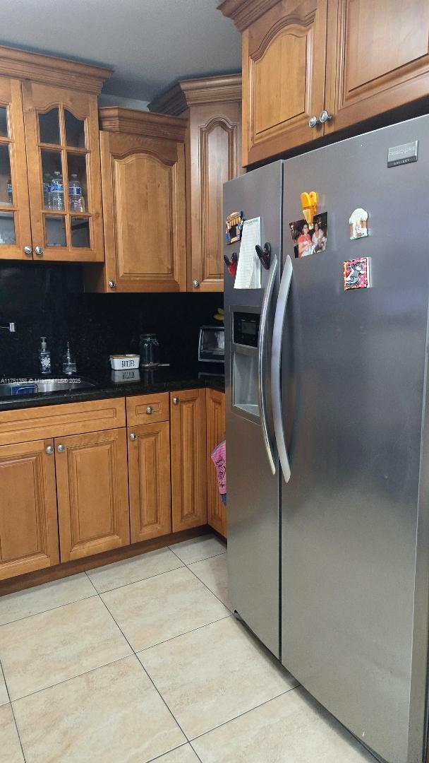 kitchen with brown cabinets, light tile patterned flooring, glass insert cabinets, and stainless steel fridge with ice dispenser