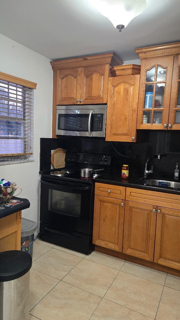 kitchen with a sink, black electric range oven, stainless steel microwave, dark countertops, and glass insert cabinets