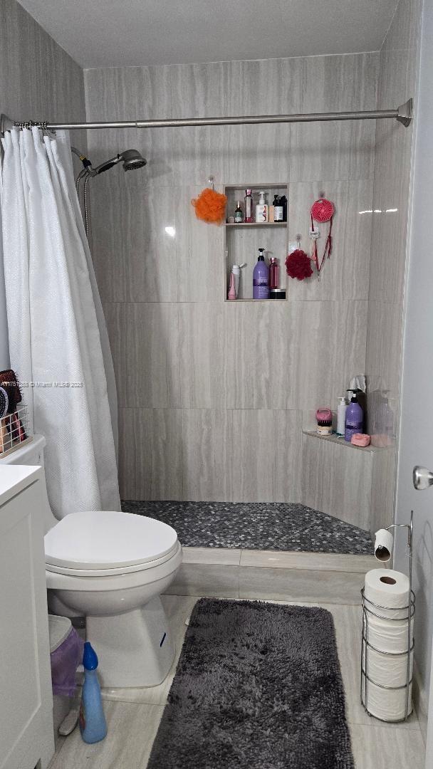 full bathroom with tiled shower, vanity, and toilet