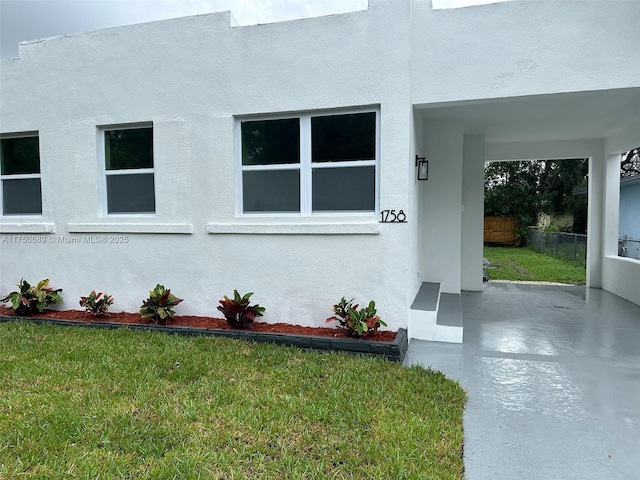 view of side of property with a lawn, fence, and stucco siding