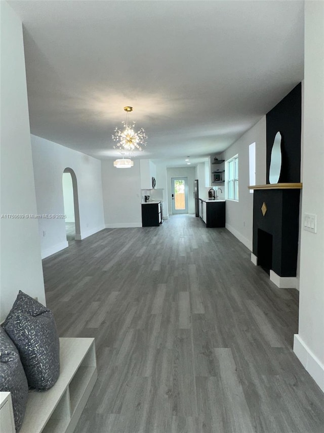 living room featuring dark wood-style floors, baseboards, arched walkways, and a notable chandelier