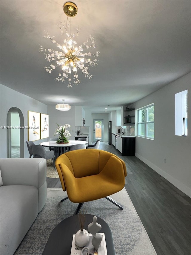 living area with baseboards, arched walkways, a notable chandelier, and dark wood finished floors