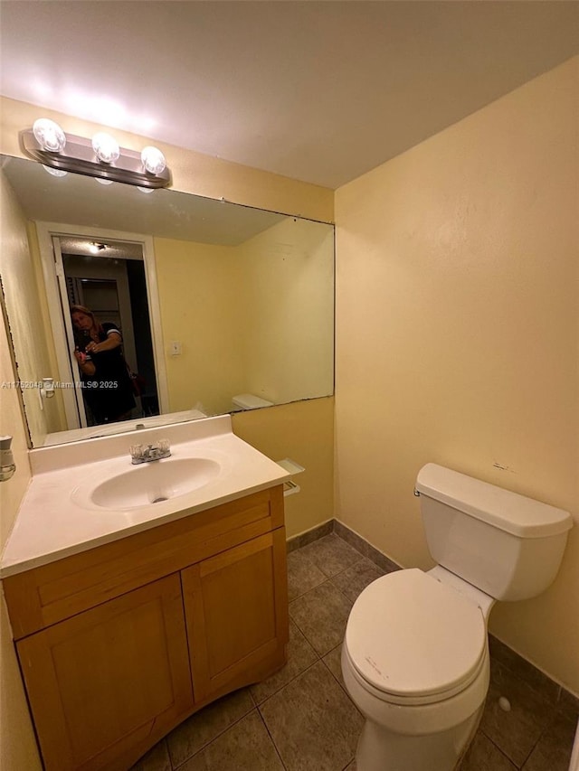 half bathroom with tile patterned flooring, baseboards, vanity, and toilet