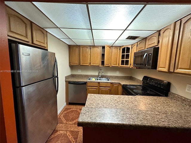 kitchen featuring a drop ceiling, a sink, light countertops, appliances with stainless steel finishes, and glass insert cabinets