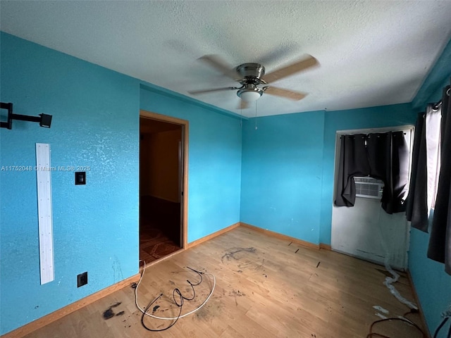 empty room featuring a textured ceiling, ceiling fan, cooling unit, wood finished floors, and baseboards