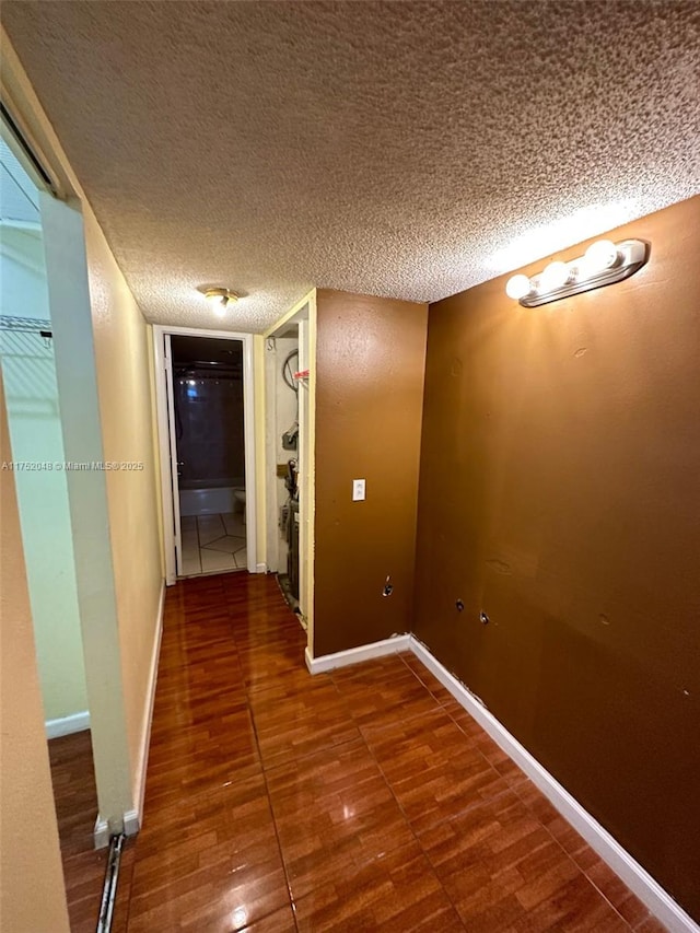 corridor with a textured ceiling, baseboards, and wood finished floors