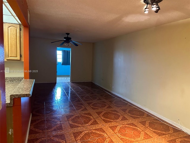 unfurnished room with a textured ceiling, ceiling fan, and baseboards