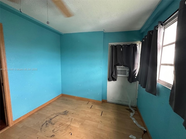 empty room with light wood-style floors, cooling unit, a textured ceiling, and baseboards