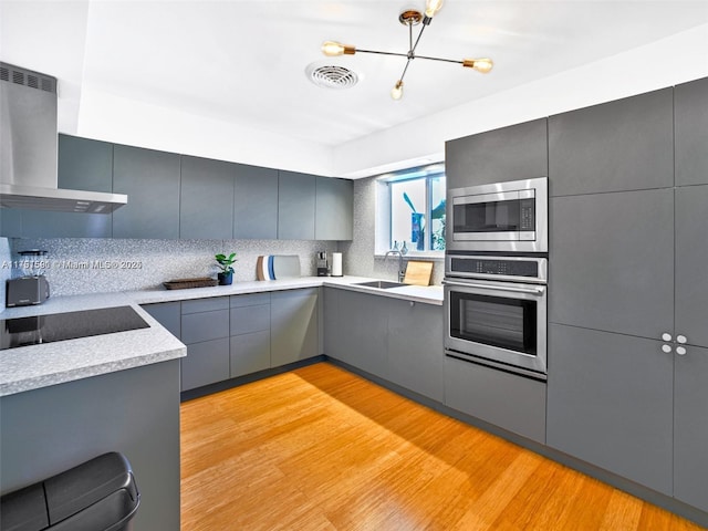 kitchen with stainless steel appliances, a sink, light countertops, wall chimney exhaust hood, and modern cabinets