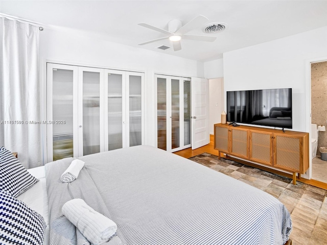 bedroom featuring a ceiling fan, visible vents, ensuite bath, and two closets