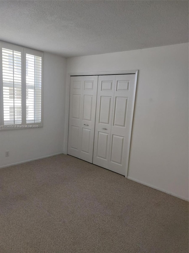 2650 S Course Dr Unit 410, Pompano Beach, FL 33069 - unfurnished bedroom featuring light colored carpet, a textured ceiling, a closet, and baseboards