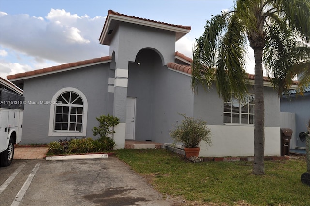 view of front facade with a front yard, a tiled roof, uncovered parking, and stucco siding