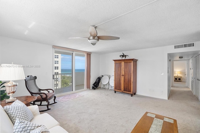 living area featuring ceiling fan, a textured ceiling, light carpet, visible vents, and a wall of windows