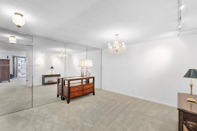 basement featuring a textured ceiling, light colored carpet, baseboards, rail lighting, and an inviting chandelier