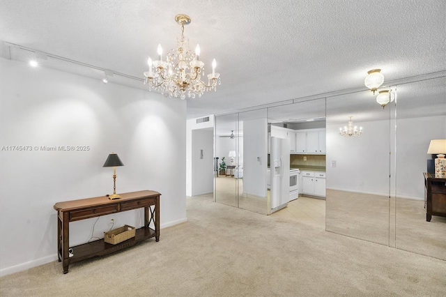 interior space with light carpet, visible vents, rail lighting, a textured ceiling, and a chandelier