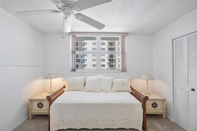 carpeted bedroom with a textured ceiling, a closet, a ceiling fan, and baseboards