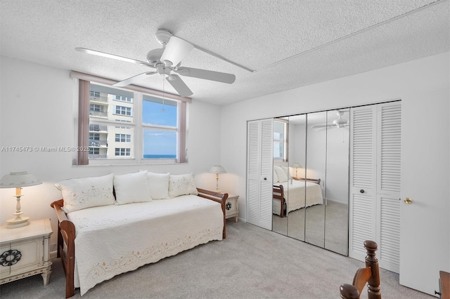 bedroom with a textured ceiling, a closet, a ceiling fan, and light colored carpet