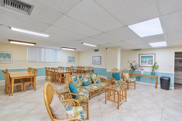 living room with light tile patterned floors, a paneled ceiling, visible vents, and baseboards