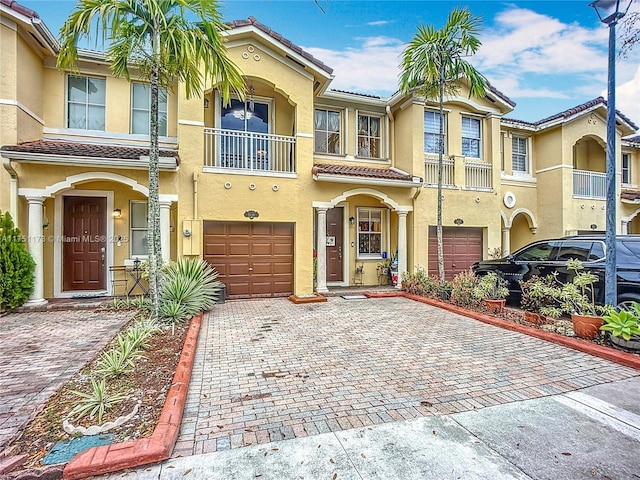 townhome / multi-family property with a tiled roof, decorative driveway, an attached garage, and stucco siding