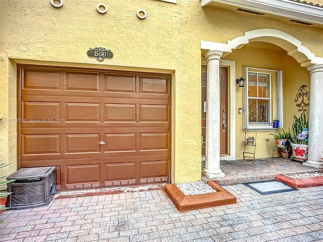 view of exterior entry featuring a garage, visible vents, and stucco siding