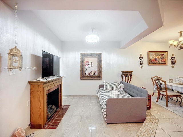 living area with light tile patterned floors, a brick fireplace, baseboards, and a chandelier