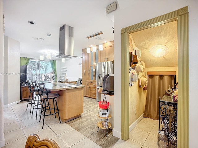 kitchen with decorative light fixtures, a kitchen island, light stone countertops, and island range hood