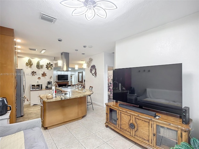 kitchen featuring a breakfast bar, visible vents, open floor plan, freestanding refrigerator, and island exhaust hood