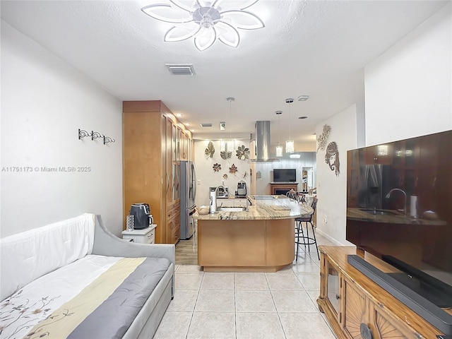 kitchen with a breakfast bar area, open floor plan, decorative light fixtures, freestanding refrigerator, and exhaust hood