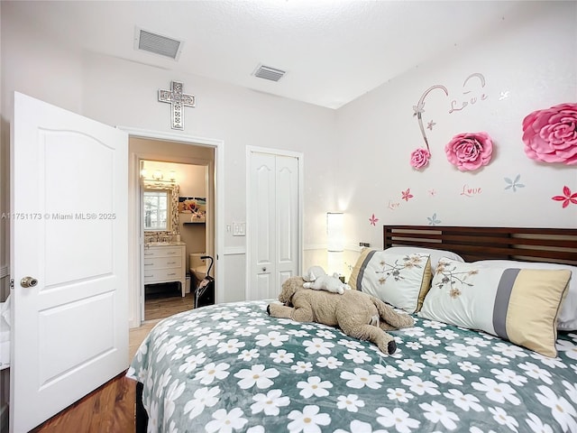 bedroom with a closet, visible vents, ensuite bathroom, and wood finished floors