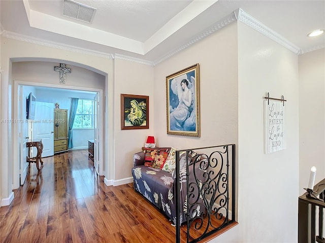 hallway with dark wood-style floors, a raised ceiling, visible vents, ornamental molding, and baseboards