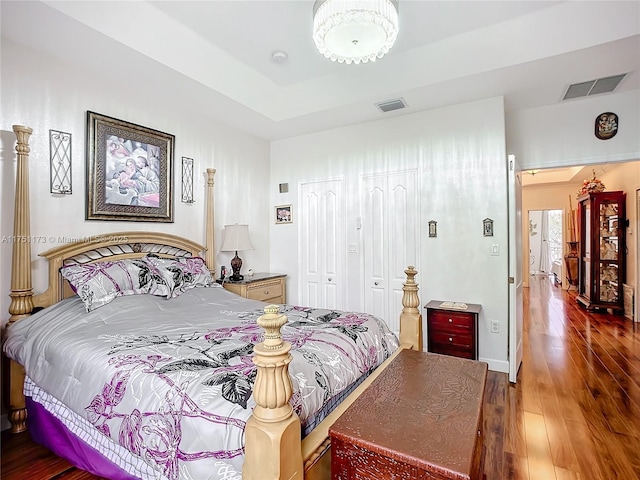 bedroom featuring a tray ceiling, a closet, visible vents, and dark wood-style flooring