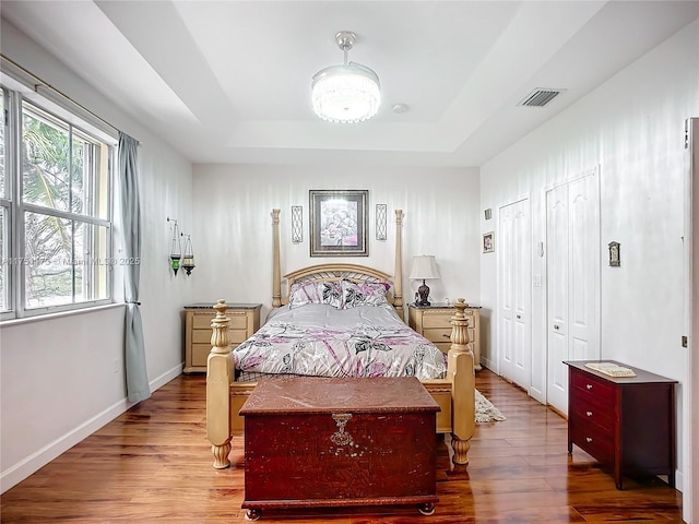 bedroom featuring baseboards, visible vents, a raised ceiling, and wood finished floors