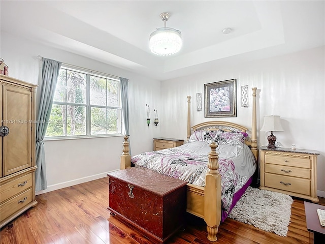 bedroom featuring baseboards, a raised ceiling, and wood finished floors