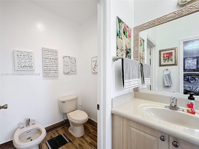 bathroom featuring toilet, a bidet, vanity, wood finished floors, and baseboards