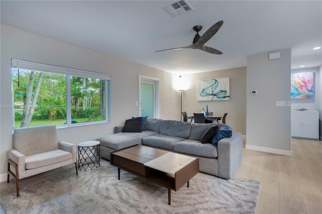 living area featuring visible vents, light wood-type flooring, a ceiling fan, and baseboards