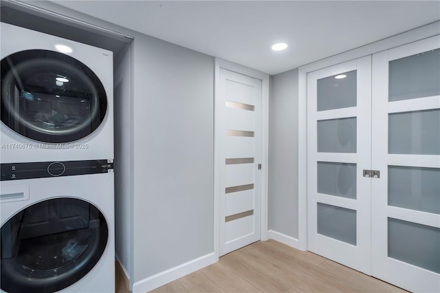 clothes washing area with light wood-style flooring, recessed lighting, stacked washer and dryer, laundry area, and baseboards