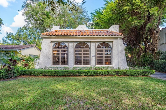 view of front facade featuring a tile roof, a front lawn, and stucco siding