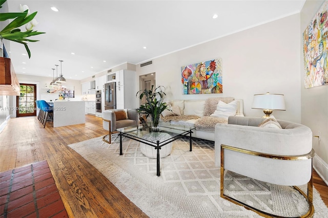 living area featuring baseboards, visible vents, crown molding, light wood-type flooring, and recessed lighting