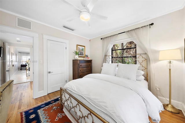 bedroom with ornamental molding, wood finished floors, visible vents, and baseboards