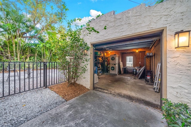 garage featuring stacked washer and clothes dryer and fence